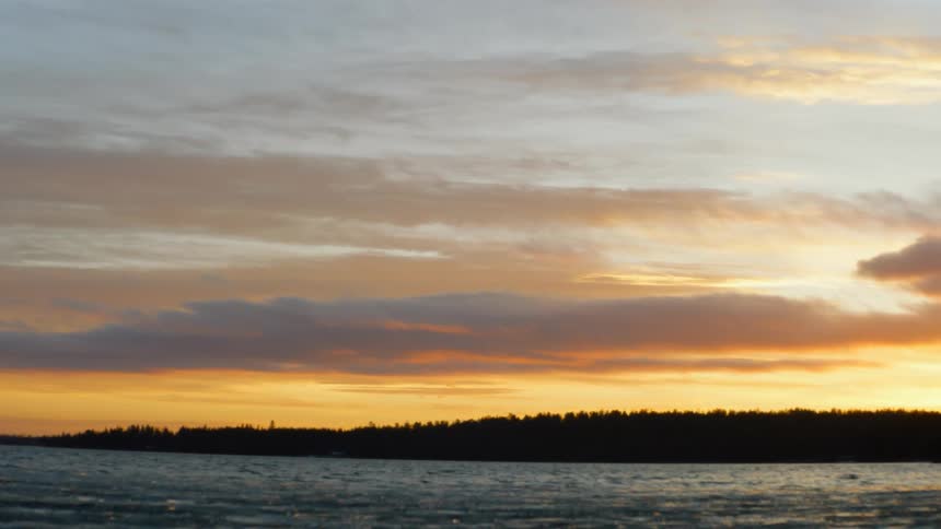 Silhouetted hill with trees next to lake at sunset