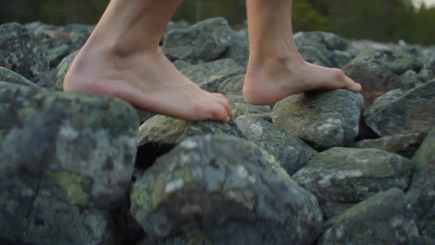 Bare feet step carefully on rocks near a river and trees