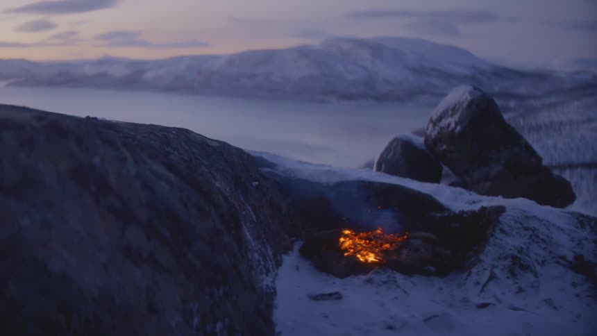 A campfire on a mountain with ice and snow with the sky and clouds in the background