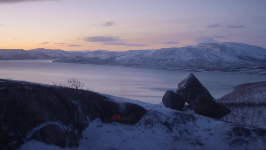Campfire over the snow near a lake on the mountains at sunset