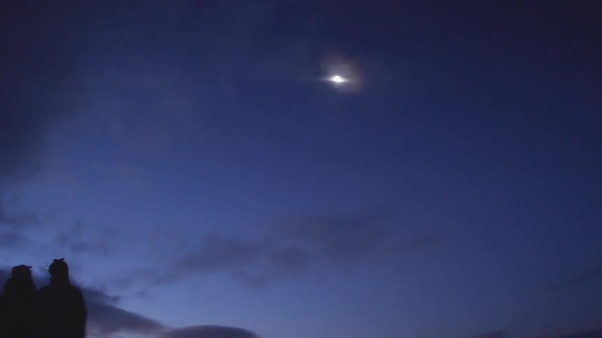 A silhouette of two people looking at the sky with the moon and clouds