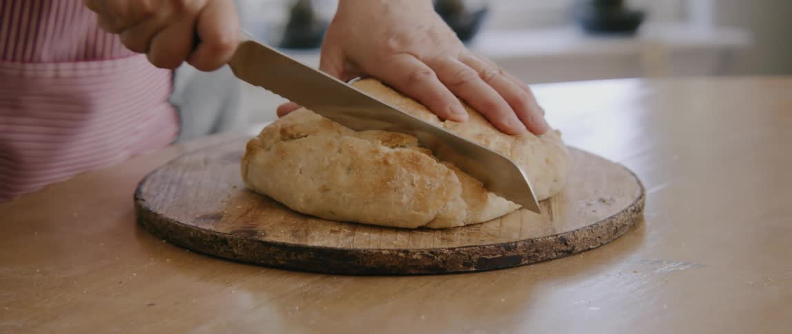 A person cutting bread with a knife on a cutting board on a table