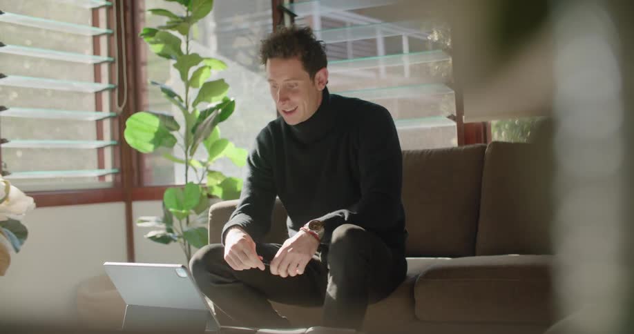 Man sits on a sofa and talks while looking at a laptop