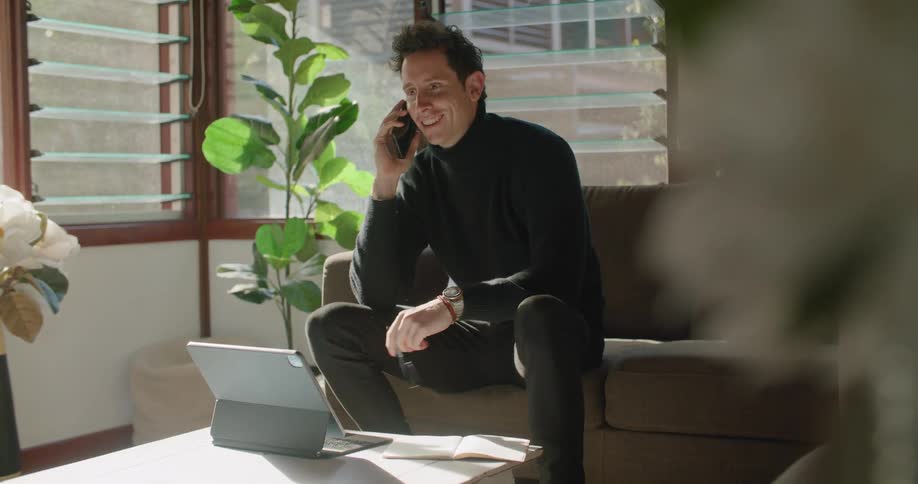 A man fidgeting with a pen while talking on a phone in a living room