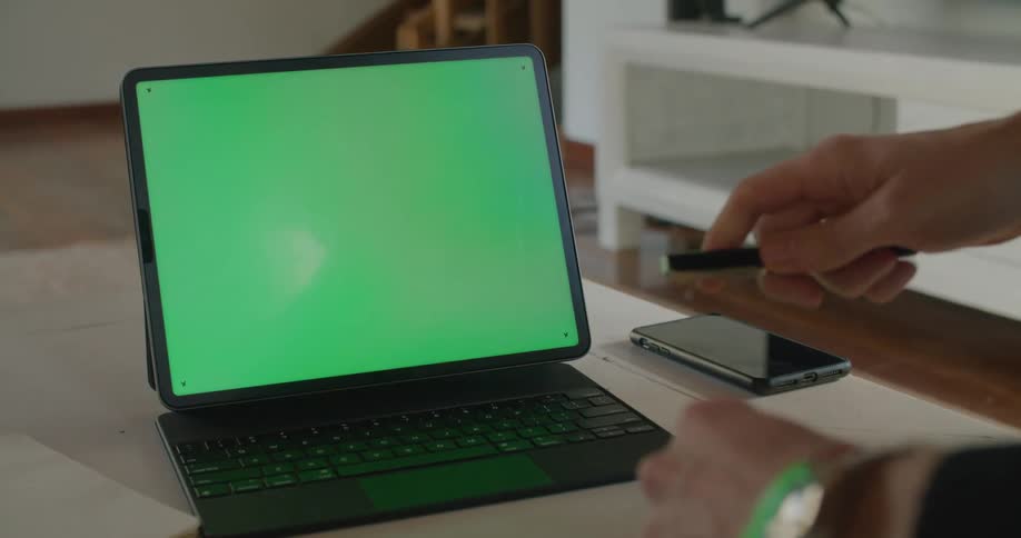 A person using a laptop on a table with a smartphone nearby