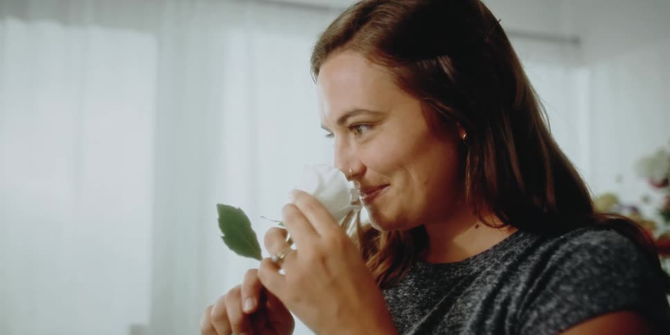 Woman opens the petals of a white rose then smells it