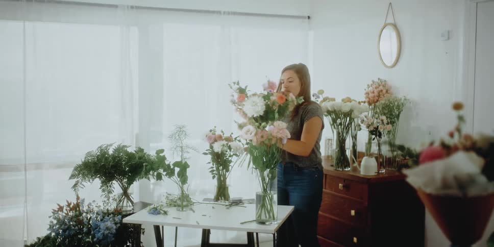 A woman arranges flower bouquets in vases in a bright white room