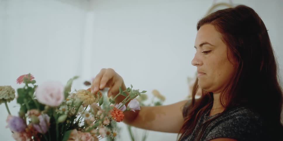 A female florist inspects individual flowers in the arrangement that she is preparing