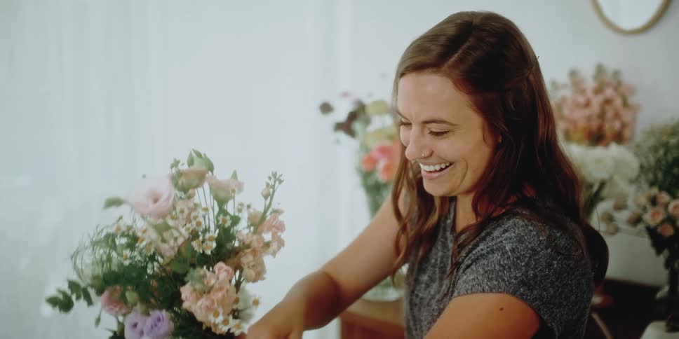 Woman smiles and holds a bouquet of flowers and adds greenery to it