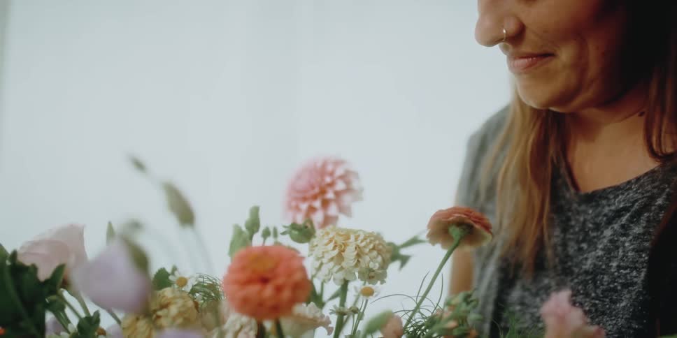 A woman with a nose piercing smiling while holding a bouquet of flowers