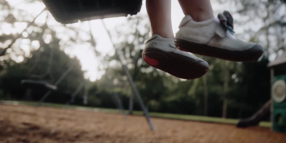 A child swinging on a swing with trees the sky and clouds in the background