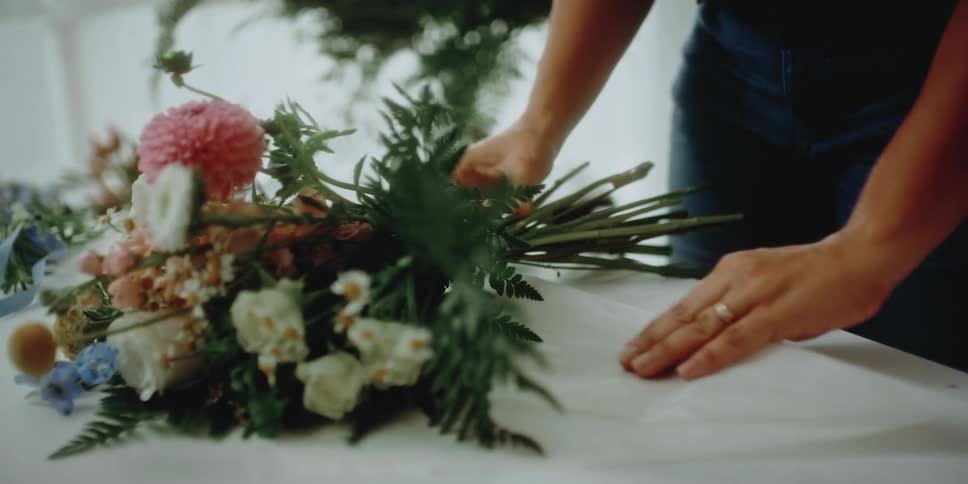 A female florist lays down a variety of flowers as she prepares a floral arrangement