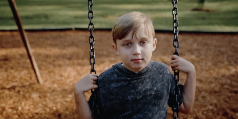 A boy swinging on a swing with grass and trees in the background