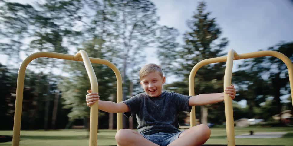 A young boy smiles as he spins around on a merrygoround at a playground