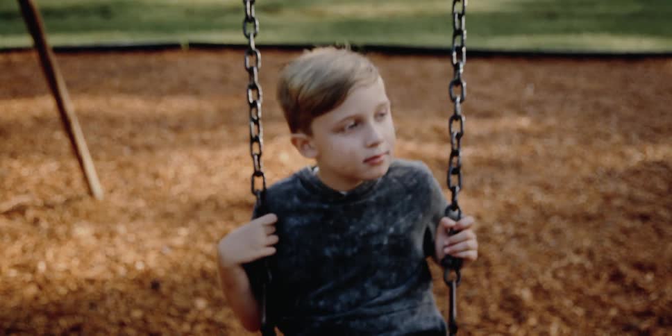 A boy leisurely swings on a swing set on a playground during the day