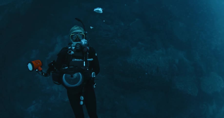 Bubbles are floating up from a diver carrying a camera underwater