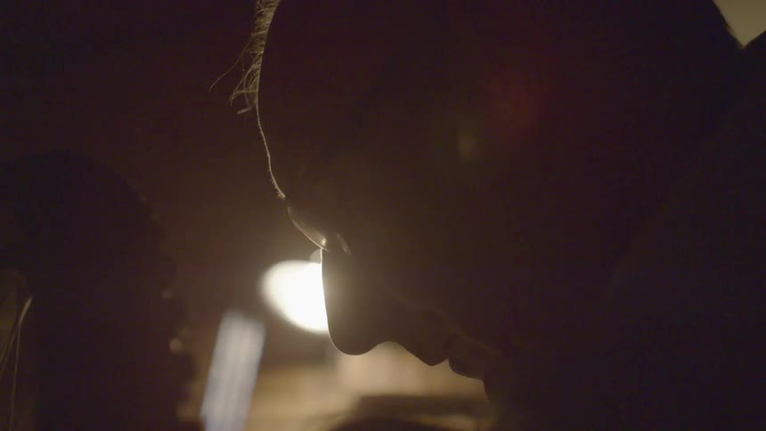 An older bald man is very close to a bicycle tire in a partially dark room
