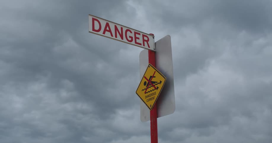Sign warning of a dangerous current under a cloud filled sky