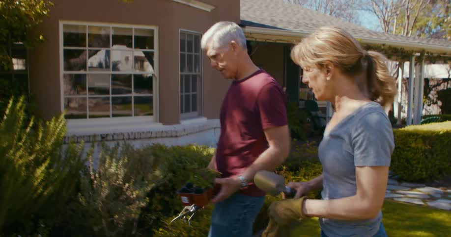 Blonde woman with ponytail and man with red shirt and jeans take care of garden