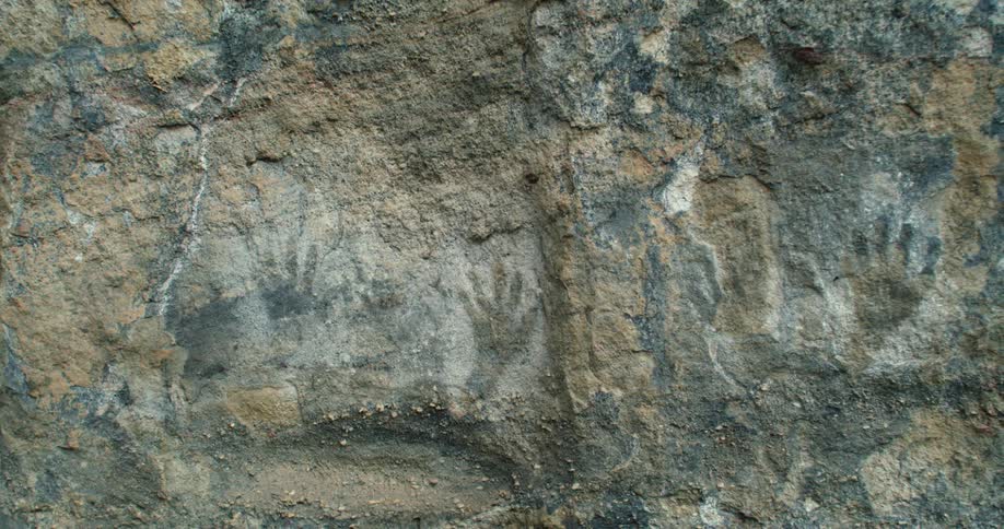 Painted hand prints are shown on a rock wall