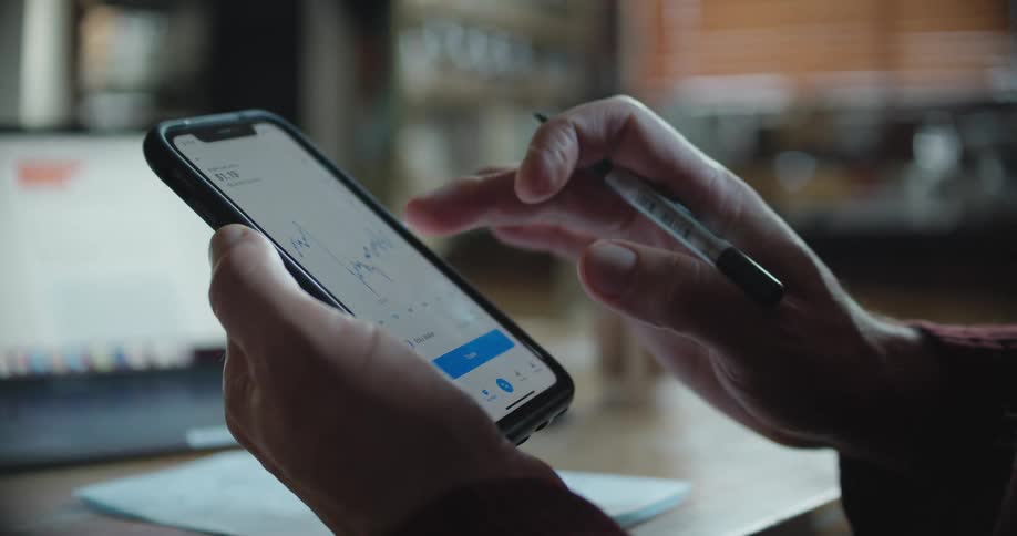 A man looks up a chart on his smart phone and jots down notes