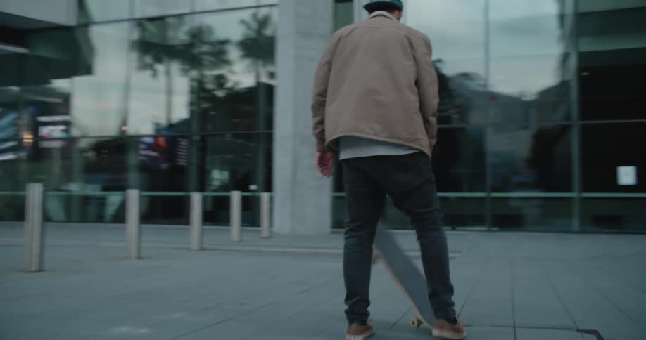 Young man driving a skateboard in the city downtown at sunset