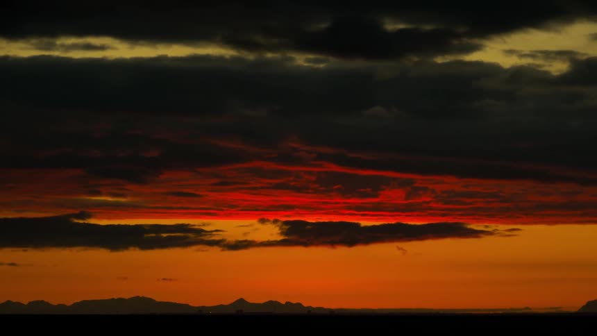 Clouds moving across a red sky with hills in the distance