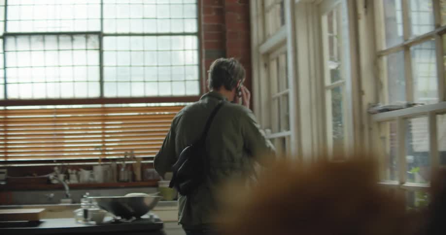 A man at home talks on the phone and empties a bag on a table and looks through a drawer