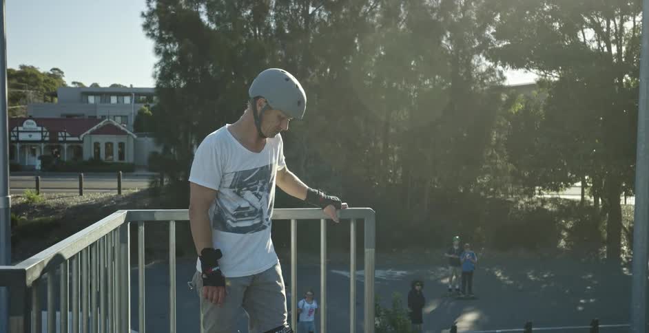 A man wearing a helmet wrist and knee pads releases the railing while people look up at him from below