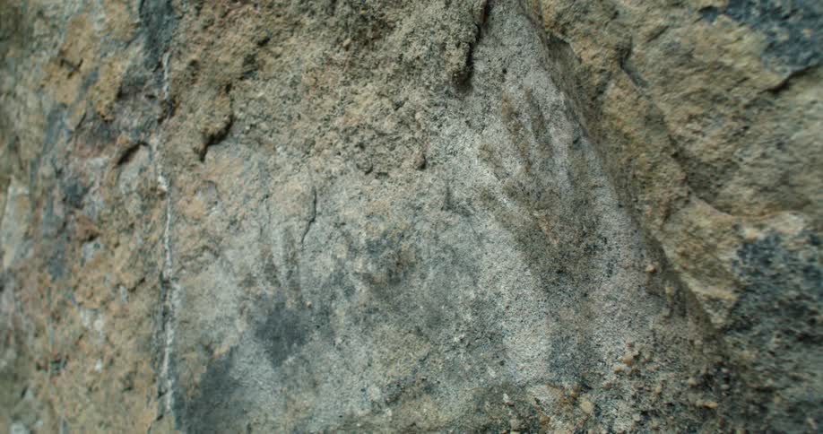 A rough and rocky surface has a faint paintings of a pair hands on it