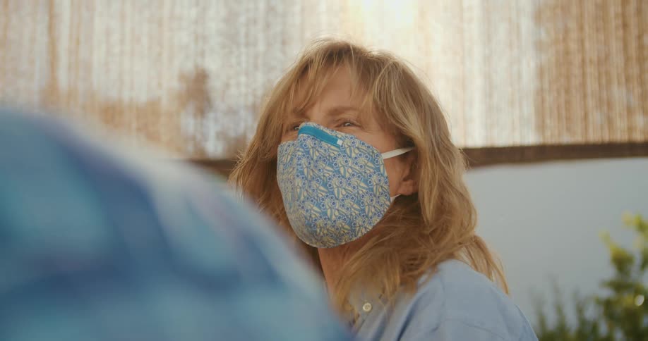 A woman adjusts the nose clip on her face mask during a conversation outside