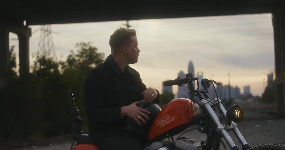 A man is sitting on a motorcycle and putting on a helmet