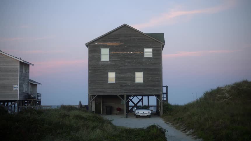 A view of the rear of two houses on a beach on a breezy day at dusk