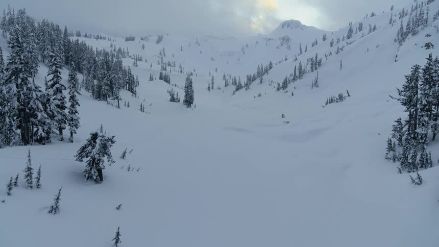 Low traverse over a narrow snow covered valley between mountains on a cloudy day