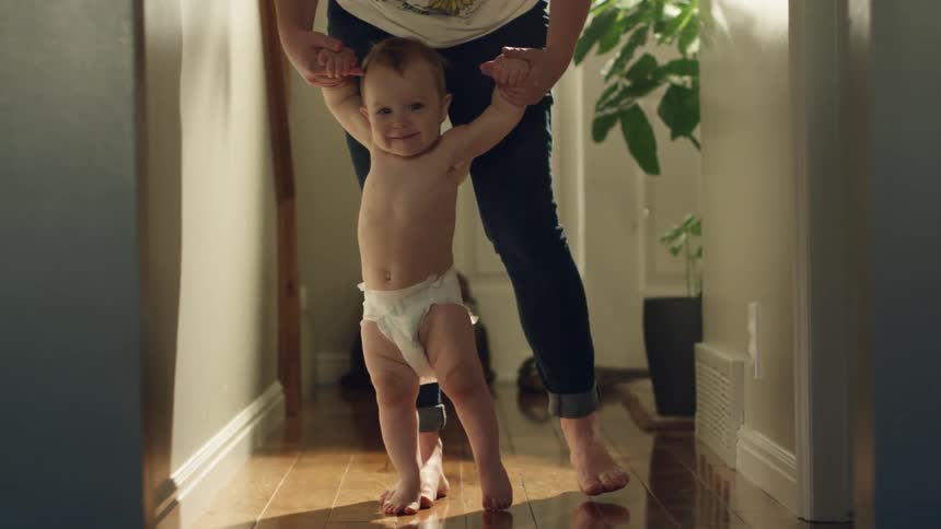 Mother teaching a toddler how to walk in a hallway at home