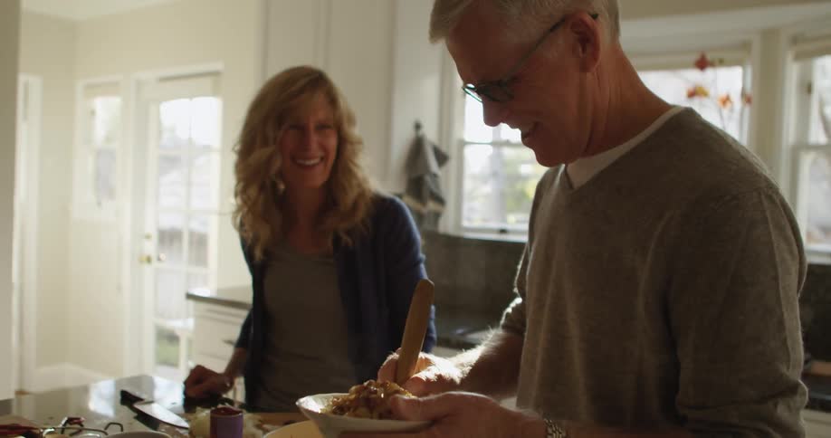 A wife and husband cooking and laughing in a kitchen during the day
