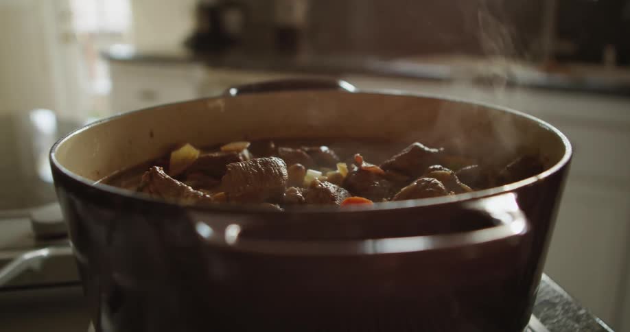 The sun shines through a window onto a steaming pot of stew on a stove