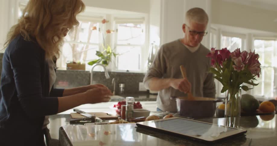 Man with glasses and grey sweatshirt stirs sauce next to blonde woman in the kitchen