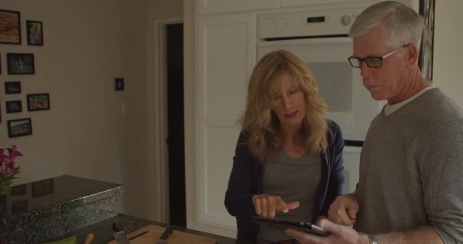 A man and woman are standing indoors and looking at cell phone