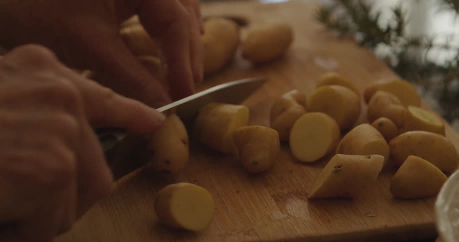 A person chopping potatoes on a cutting board with a sharp knife