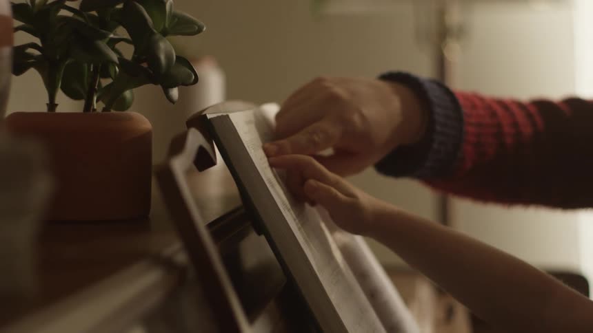 An adult sits with a child at a piano teaching him to read music