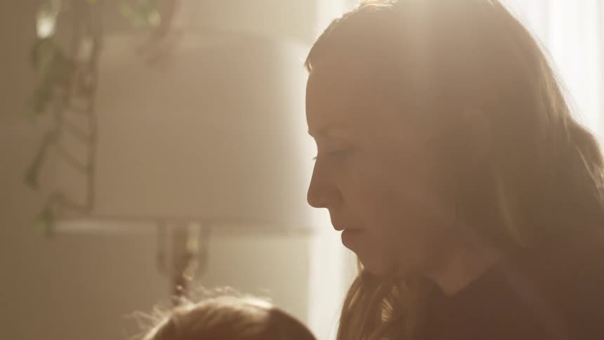 A woman with a child in a room with a lamp a wall and a window in the background