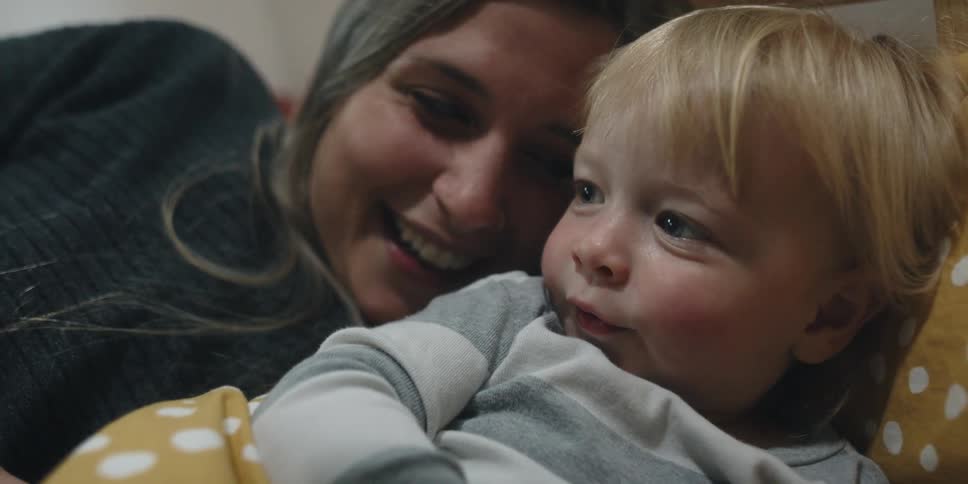 Mother and child lie on bed together smiling and talking