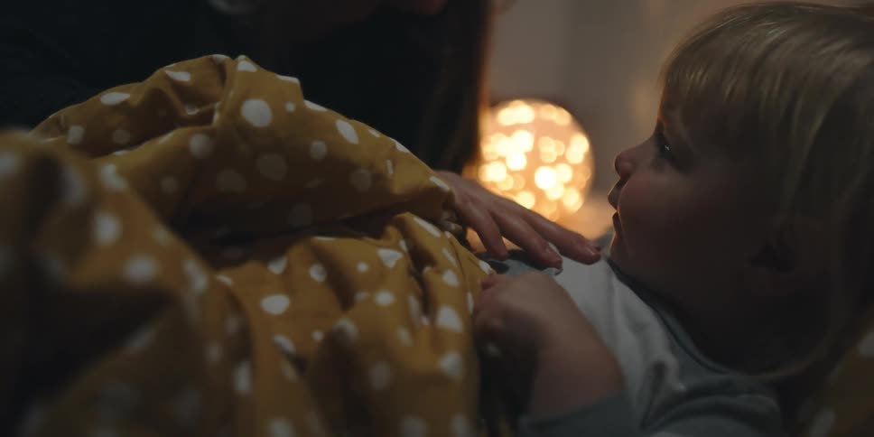 A mother tucks her son into bed and brushes his face with her finger