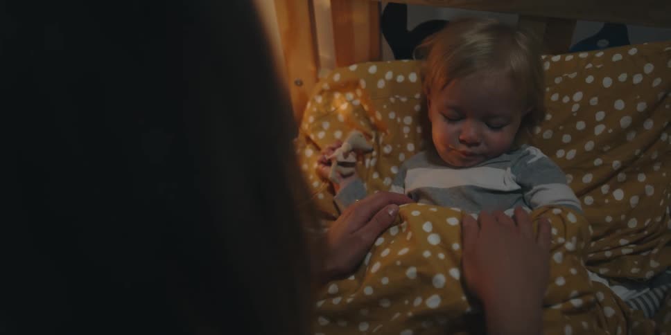 A mother tucks her son into bed and brushes her hand across his face