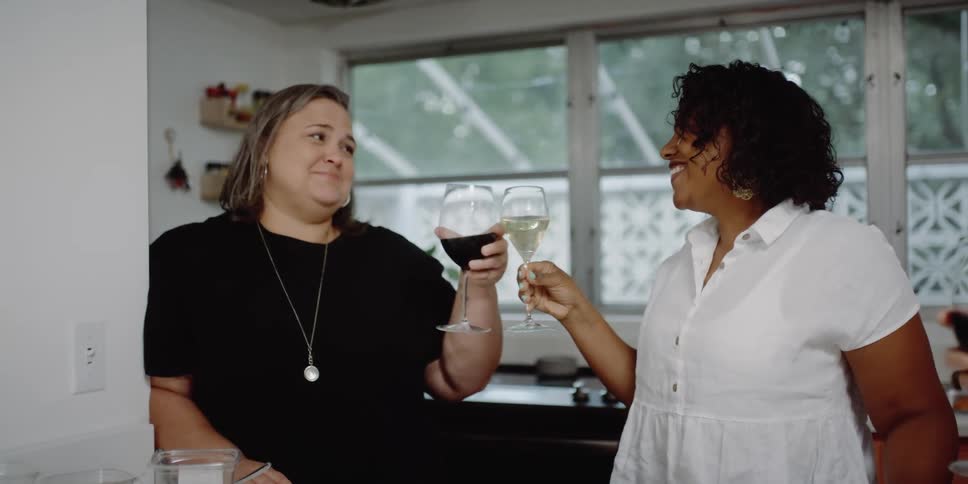 Women smile and laugh while drinking wine in a kitchen