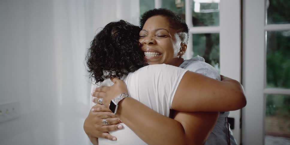 Three women in a room with one enter in a door and hugging another woman