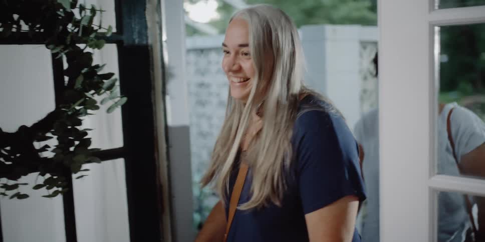 A woman opens a door and greets her visitors with a hug