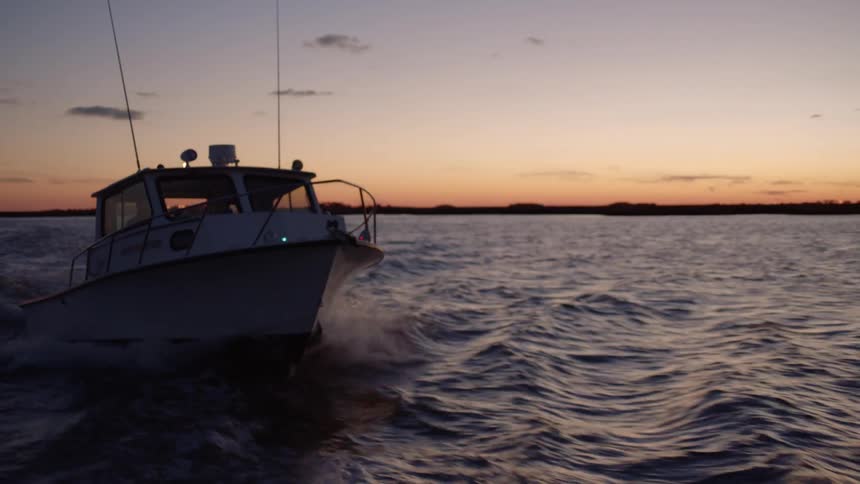 A fast motorboat driving past camera at sunset