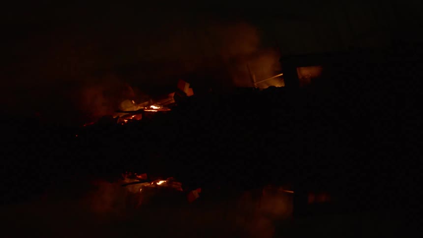 A fire burning at night with water on the ground nearby